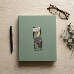 The Siren Climbs Aboard Odyssey bookmark flat lay on a desk with a book, pen and reading glasses