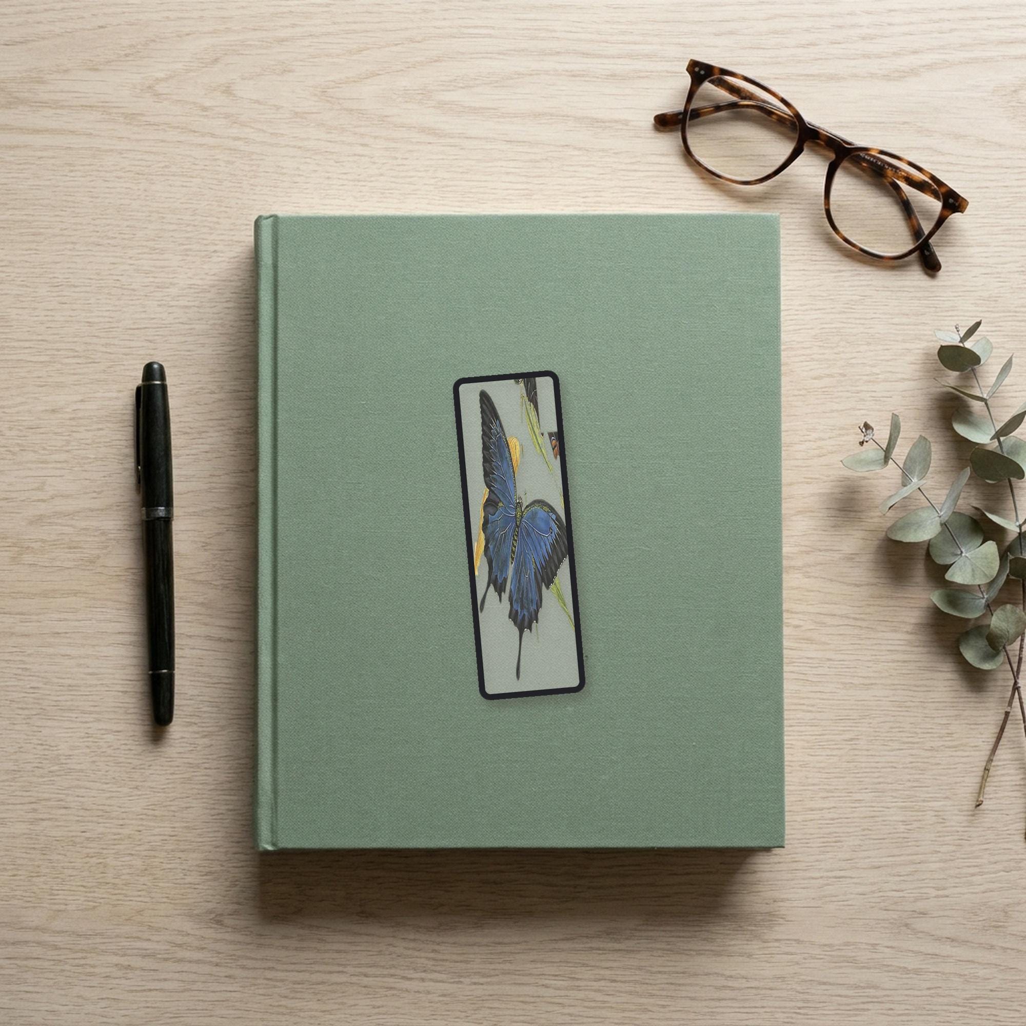 The Ulysses Butterfly Odyssey bookmark flat lay on a desk with a book, pen and reading glasses