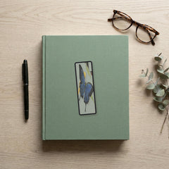 The Ulysses Butterfly Odyssey bookmark flat lay on a desk with a book, pen and reading glasses