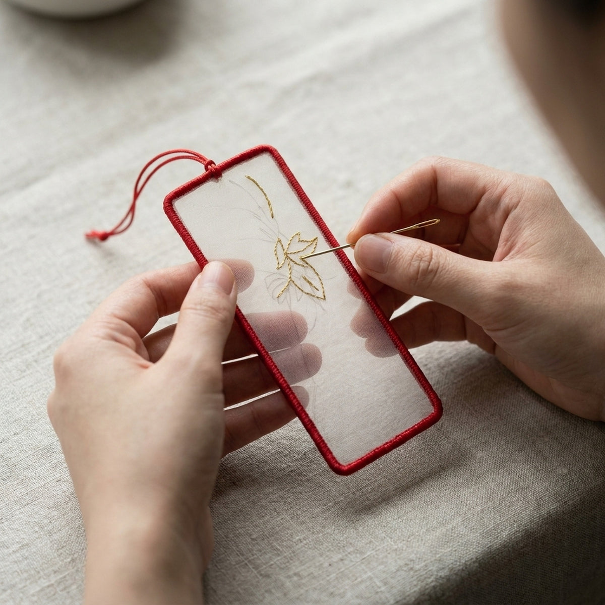 Stitching a leaf in fine silk thread on the bookmark blank, held by its cord edge without a hoop