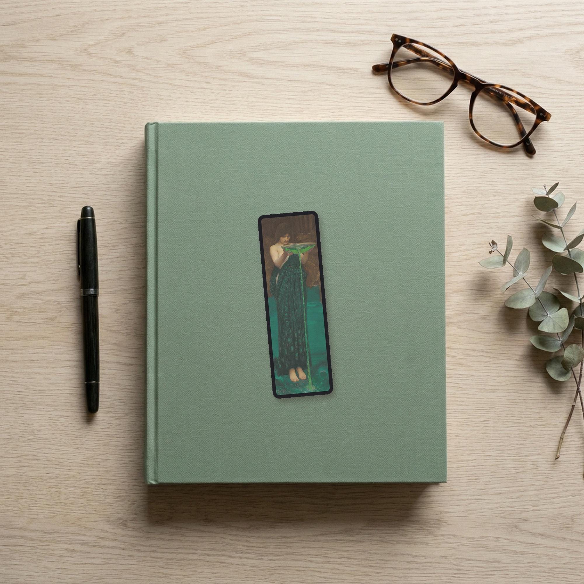 The Poisoner of the Sea Odyssey bookmark flat lay on a desk with a book, pen and reading glasses