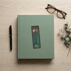 The Poisoner of the Sea Odyssey bookmark flat lay on a desk with a book, pen and reading glasses