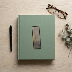 Escape at Dawn Odyssey bookmark flat lay on a desk with a book, pen and reading glasses