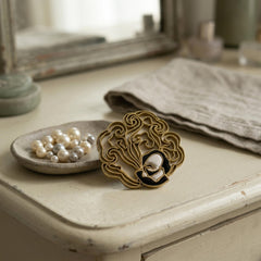 The lucky cloud brooch on a dressing table beside a dish of pearls (scene staged around a photograph of the real brooch)