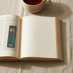 The Poisoner of the Sea Odyssey bookmark lying on an open book, the page text visible through the sheer organza