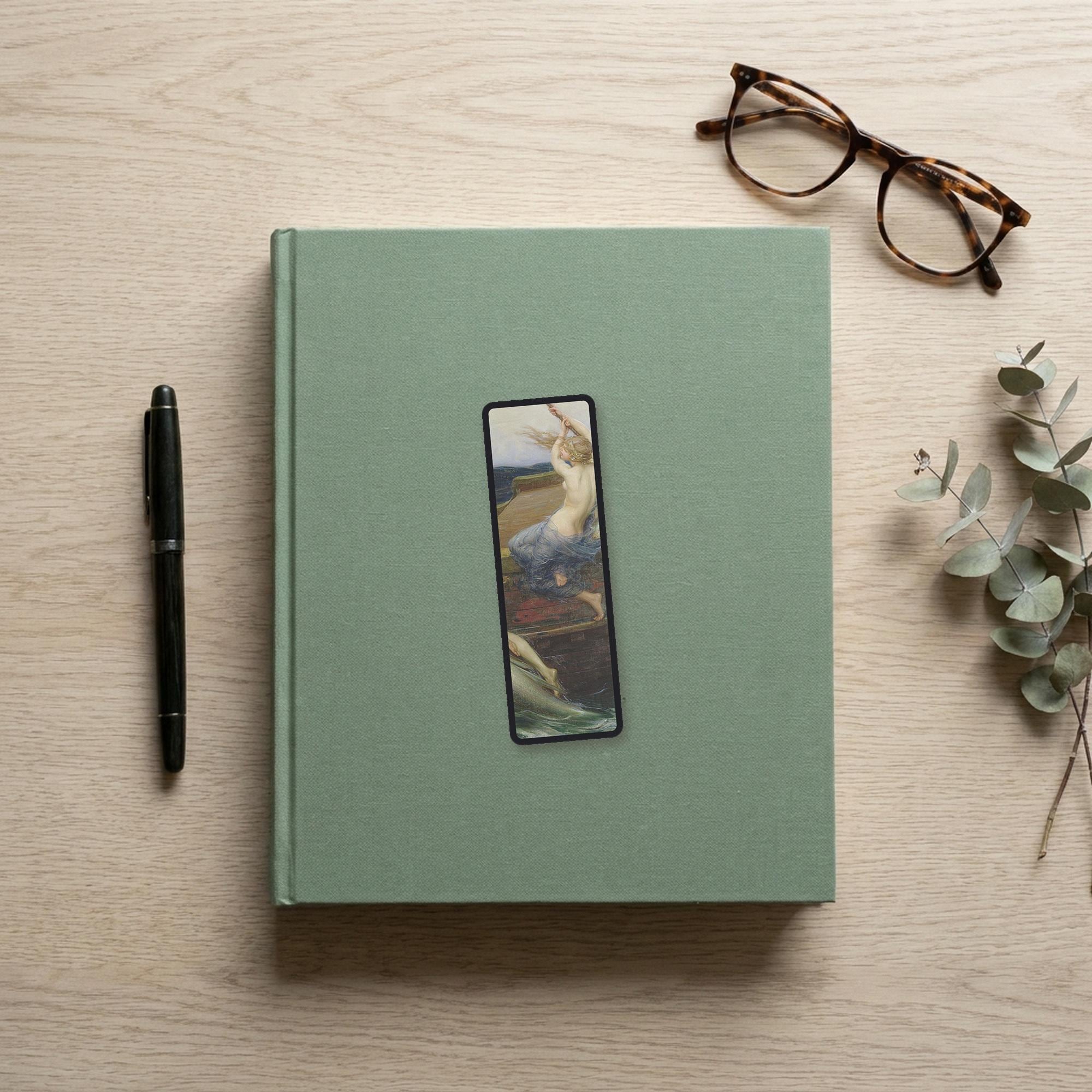 The Siren Climbs Aboard Odyssey bookmark flat lay on a desk with a book, pen and reading glasses