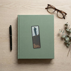 The Wanderer Odyssey bookmark flat lay on a desk with a book, pen and reading glasses